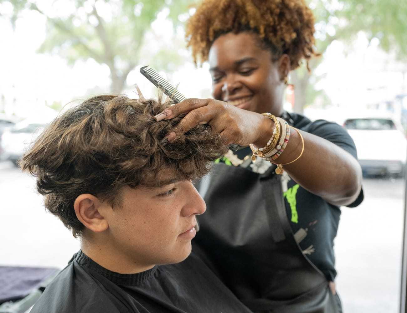 A stylist trims a young man's hair at a salon.