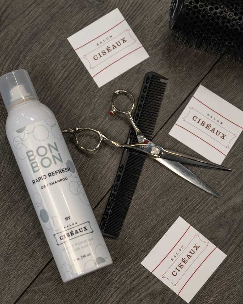 Dry shampoo, scissors, and comb on salon cards and countertop.