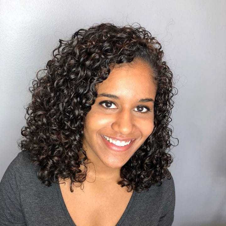 Curly-haired woman smiling with a grey background.