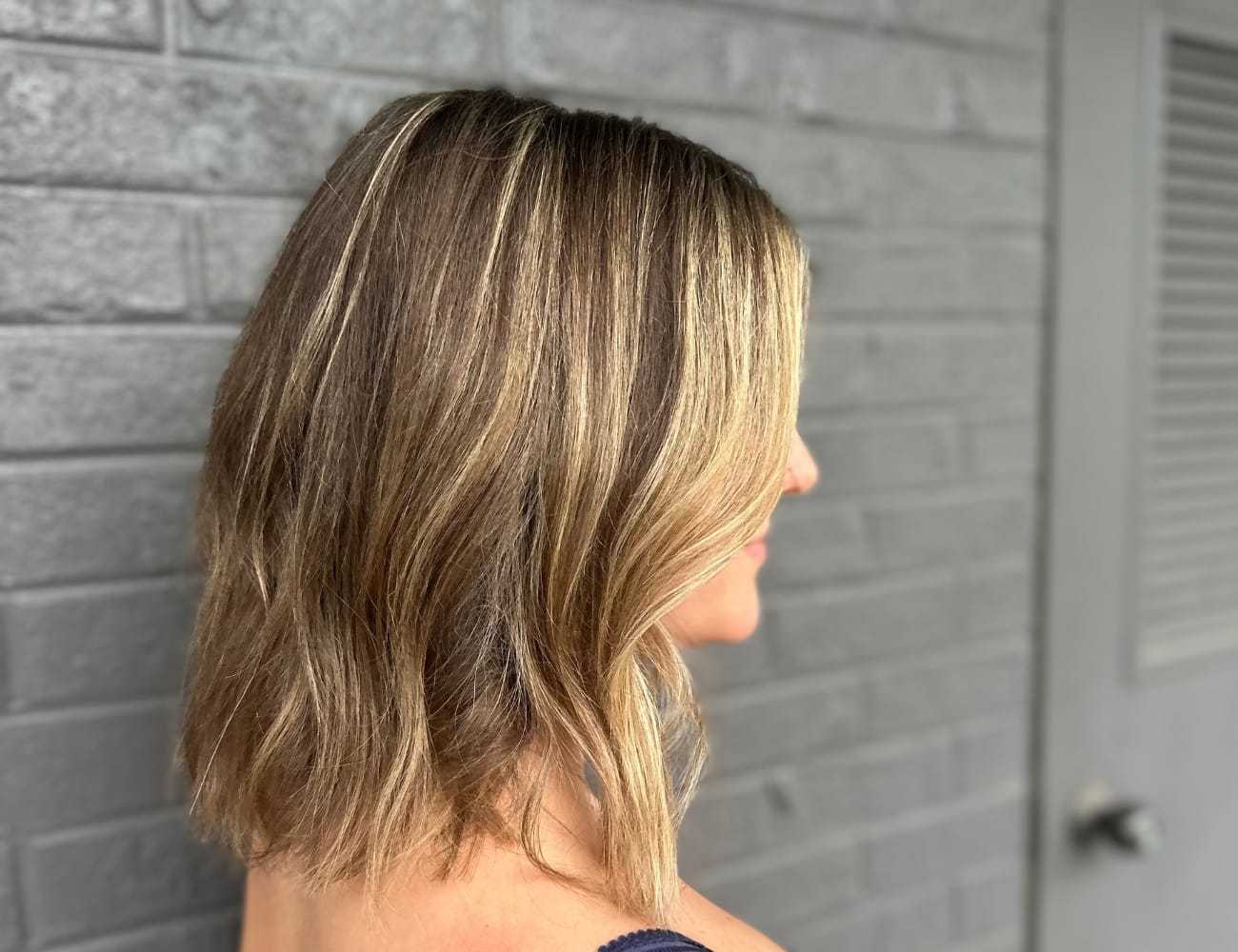 Short, wavy bob hairstyle with blonde highlights against a gray brick wall.