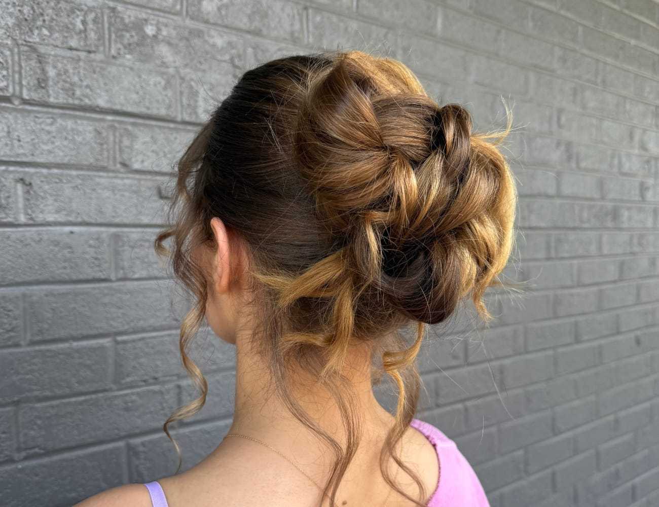 Elegant updo hairstyle with loose curls against a gray brick wall.