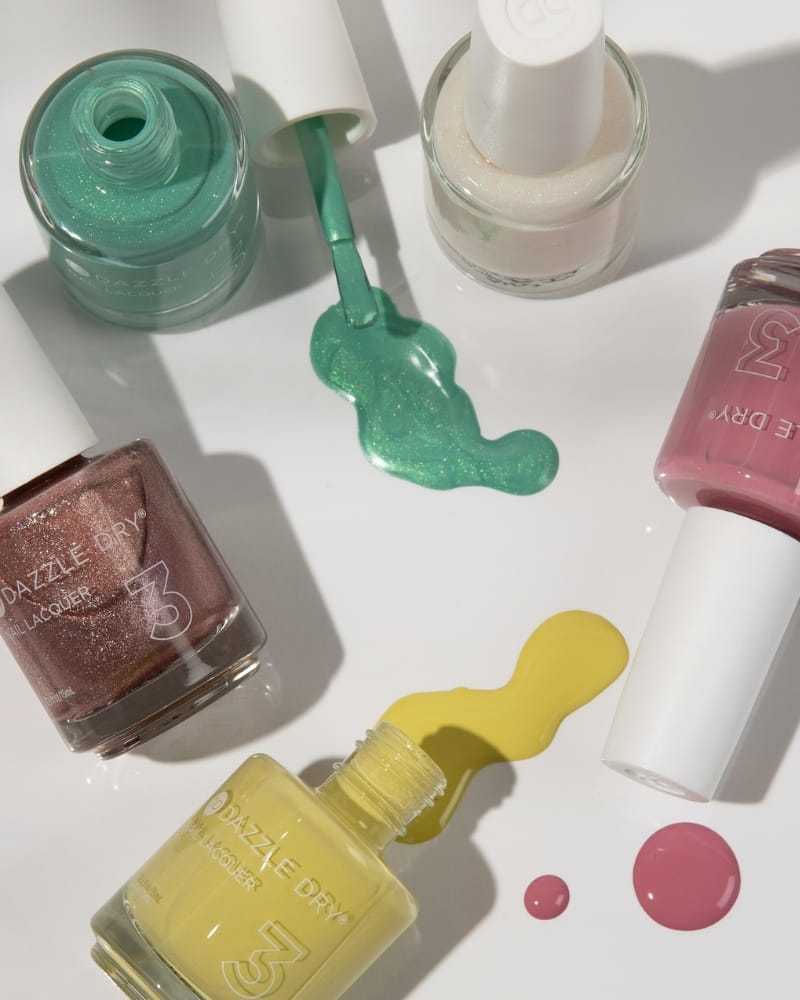 Colorful nail polish bottles with spilled paint on a white surface.
