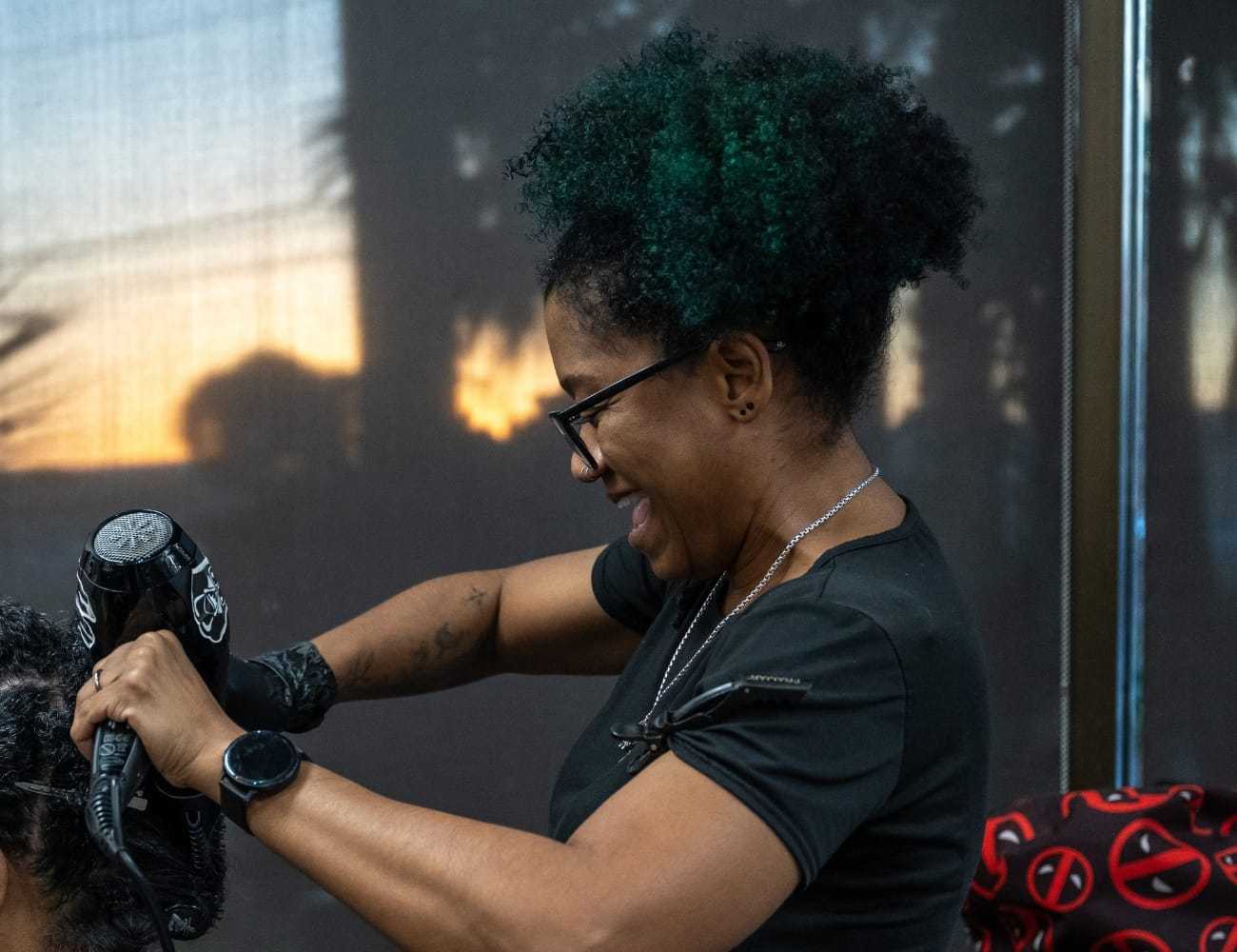 Woman styling hair with a blow dryer during sunset indoors.
