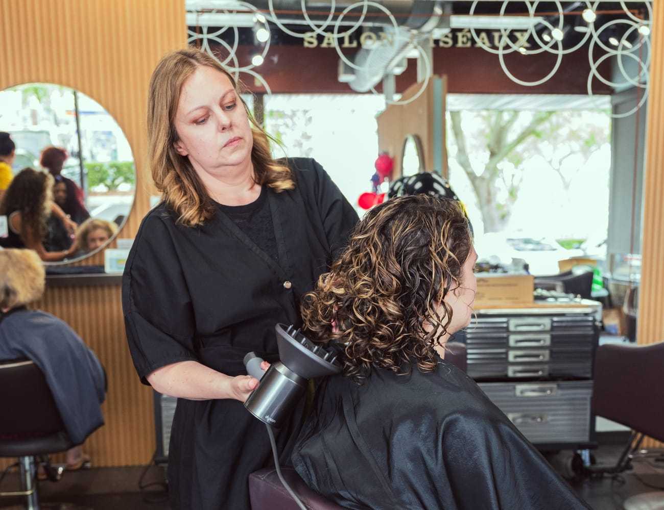 Hairdresser styling curly hair with a diffuser in a salon.