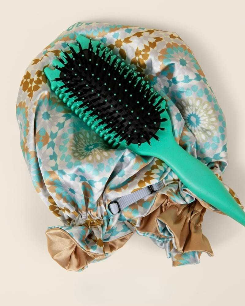 Shower cap with floral pattern and a green hairbrush on a beige background.